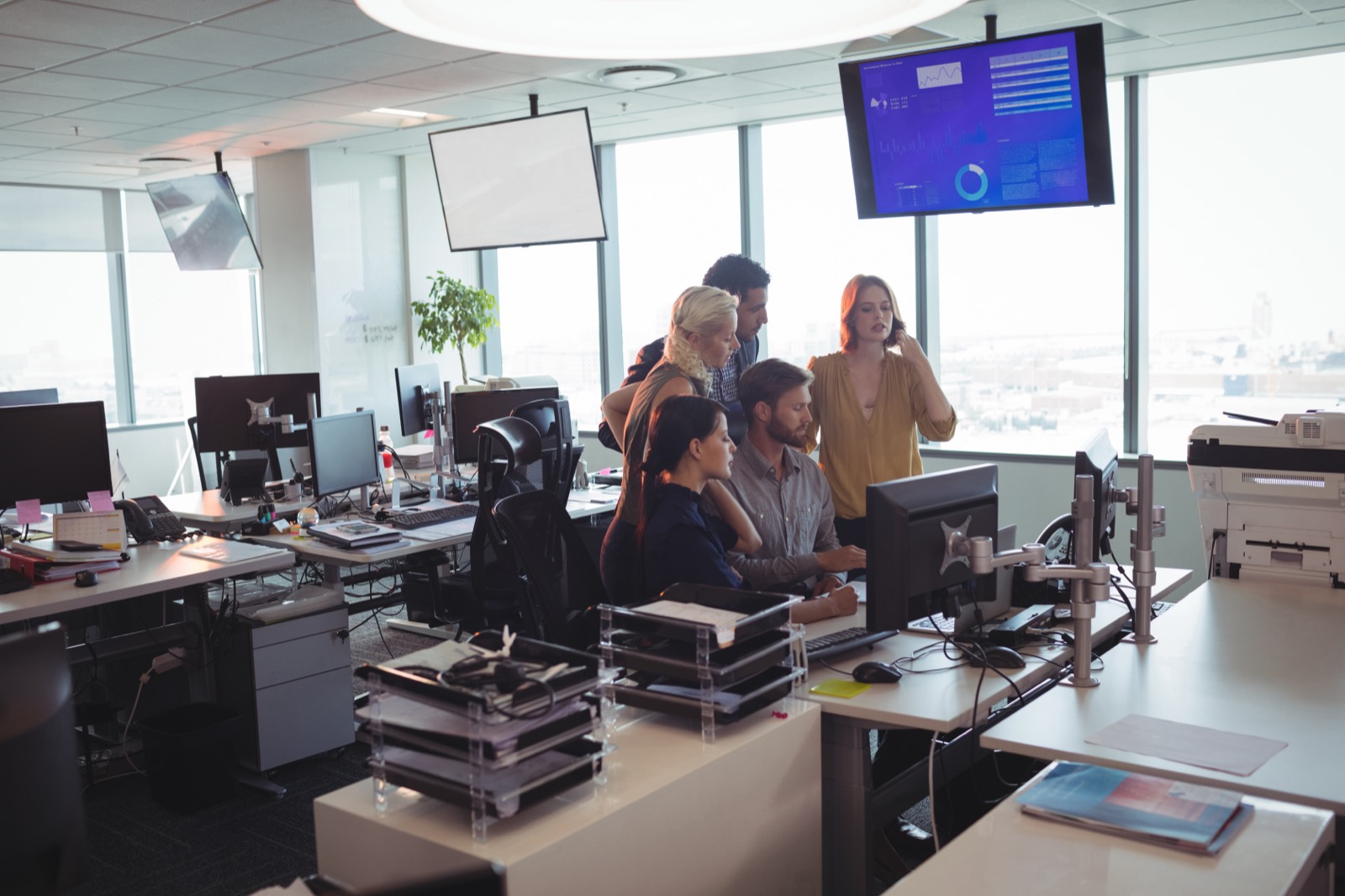 Office team gathered around a workstation, one colleague taking a phone call.