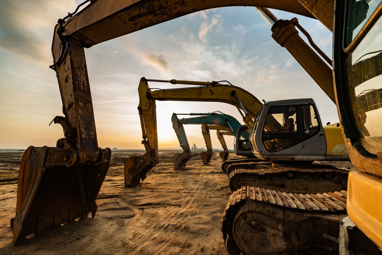 Row of excavators parked idle in an equipment yard at sunset.
